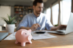 Man calculates expenses pay bills use laptop, focus on piggybank