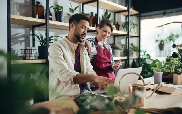 Small business owners discussing debt management strategies while working on a laptop in a plant shop
